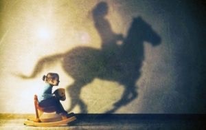 Bambina su un cavallo a dondolo con l'ombra di un cavallo vero, sostegno e psicoterapia in età evolutiva